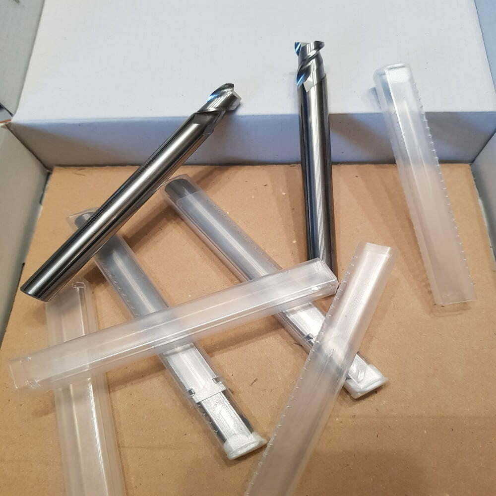 Juego de fresas de metal en un embalaje de cartón, con varias fresas y sus fundas protectoras transparentes. Ideal para trabajos de mecanizado y fresado.