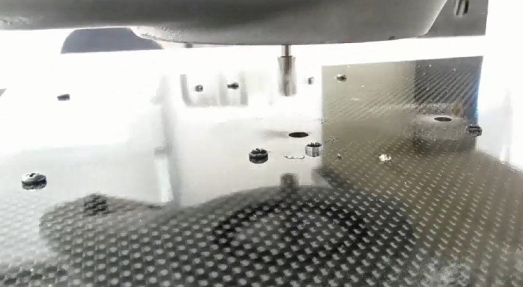 Imagen de una máquina de fresado CNC enfocada en la herramienta de corte, mostrando la superficie de trabajo con agujeros y residuos de material. Ideal para ilustrar procesos de mecanizado y fabricación de precisión.