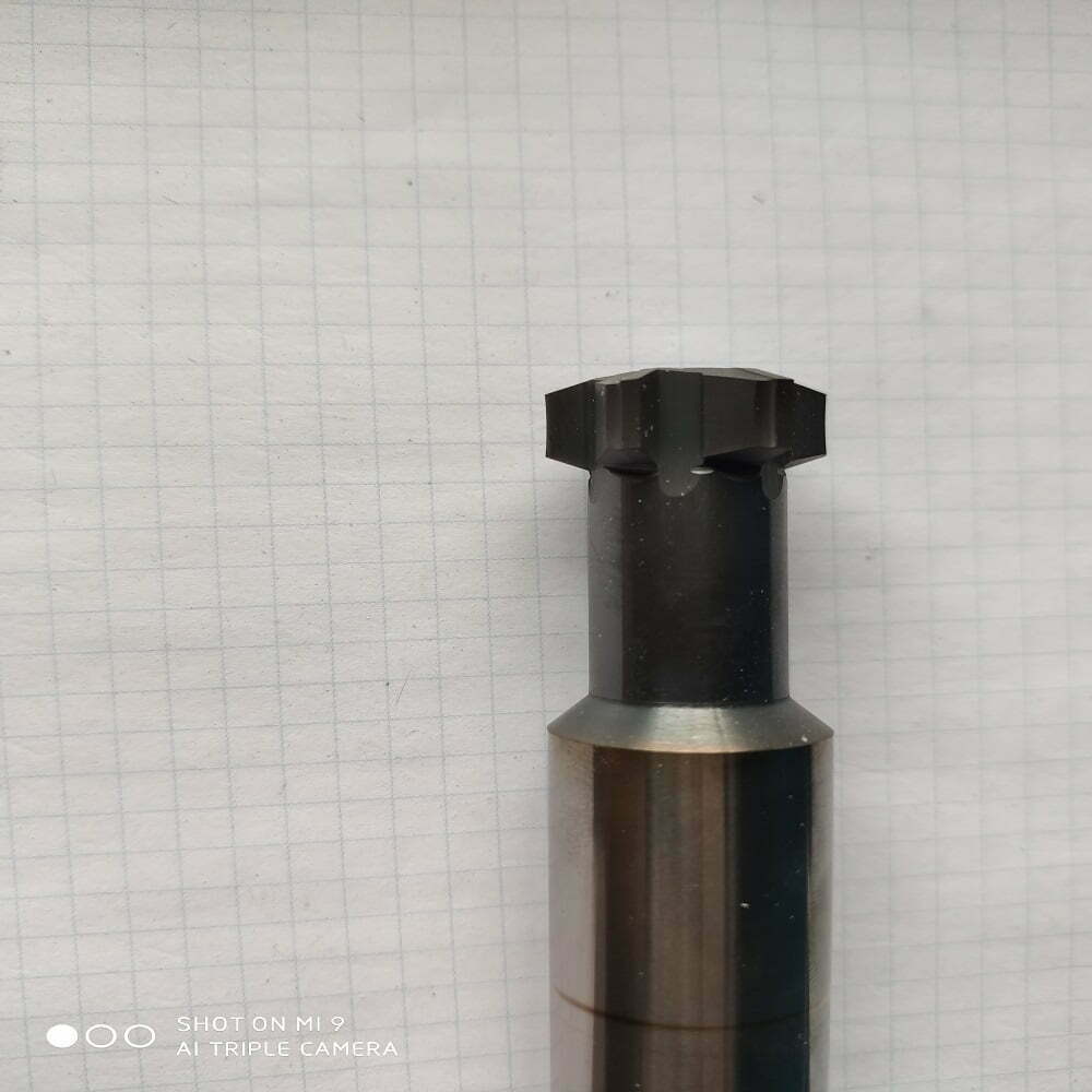 Herramienta de corte de metal con diseño hexagonal en la parte superior, sobre fondo de papel cuadriculado.