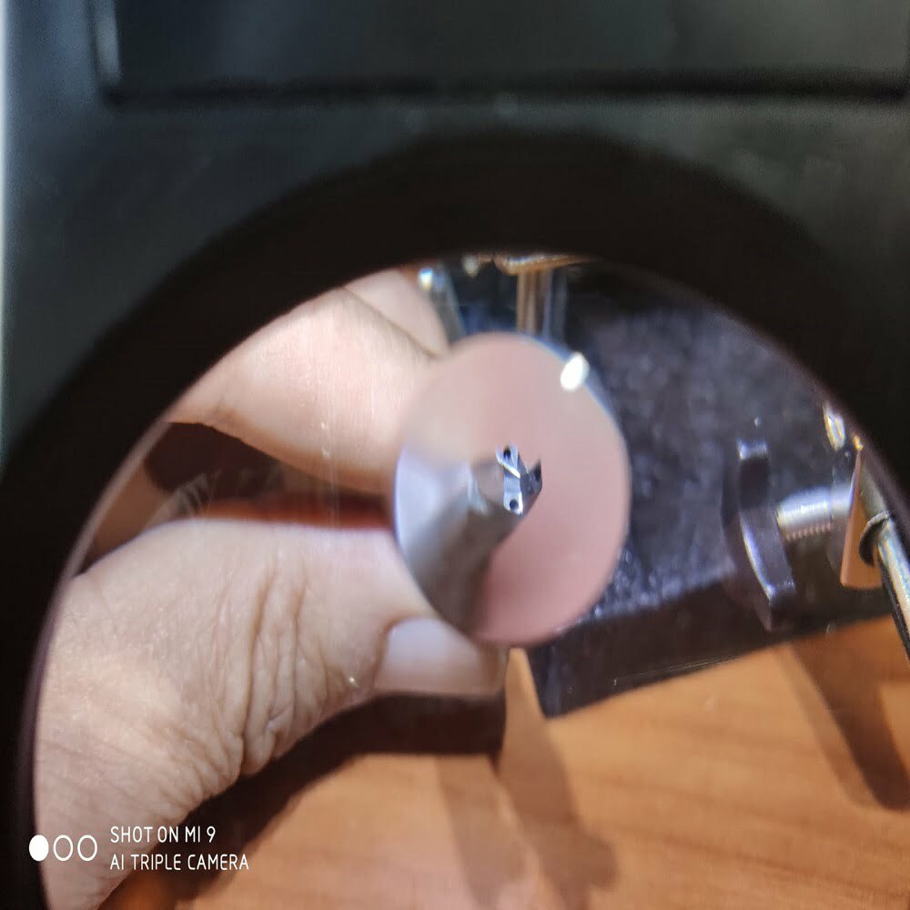 Imagen en primer plano de una herramienta de precisión observada a través de una lupa, mostrando detalles del extremo de la herramienta y la mano que la sostiene, sobre un fondo de superficie de trabajo.