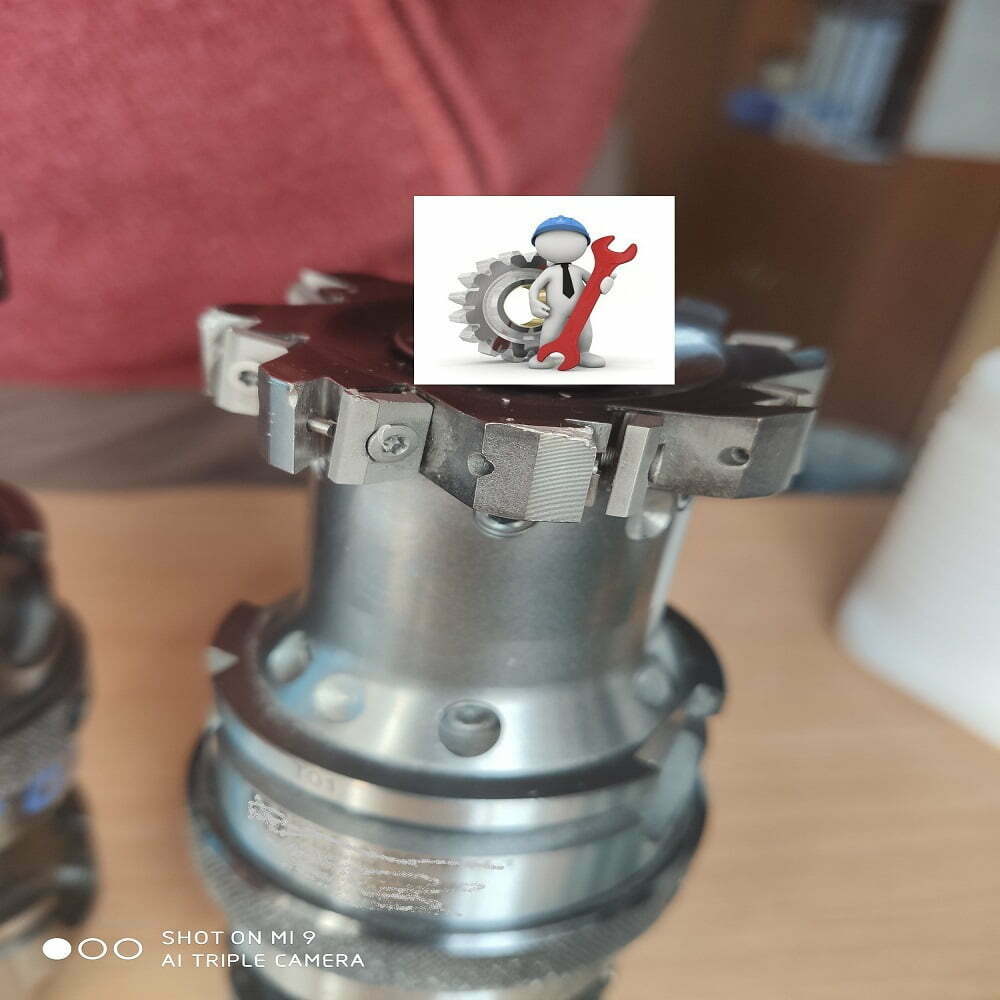Imagen de un componente mecánico de precisión con un engranaje y un diseño detallado, sobre una superficie de trabajo. Incluye un ícono de figura técnica sosteniendo una llave inglesa, representando mantenimiento o reparación.