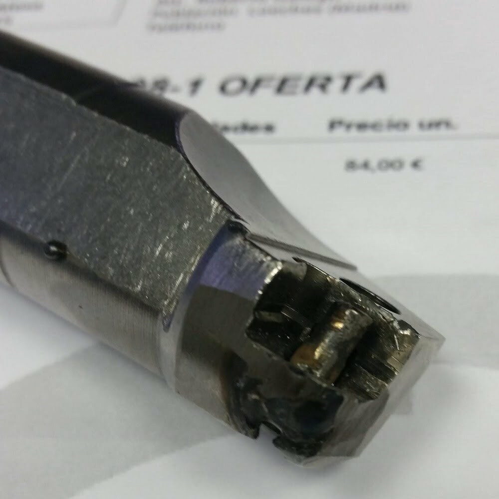 Imagen de un accesorio metálico para herramientas, mostrando un detalle del extremo con desgaste visible. En el fondo, se observa un documento con la palabra "OFERTA" y un precio de 4,00 €.