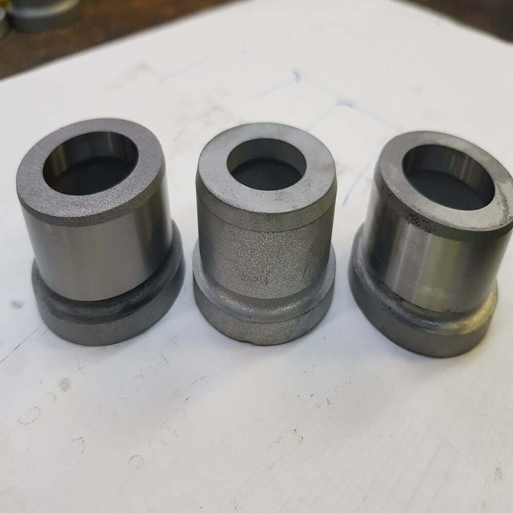 Tres piezas metálicas cilíndricas con acabado pulido, utilizadas en aplicaciones industriales, sobre una superficie de trabajo.